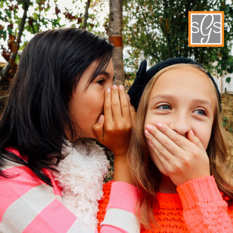 Kid whispering at her friend that is trying to hold her laugh