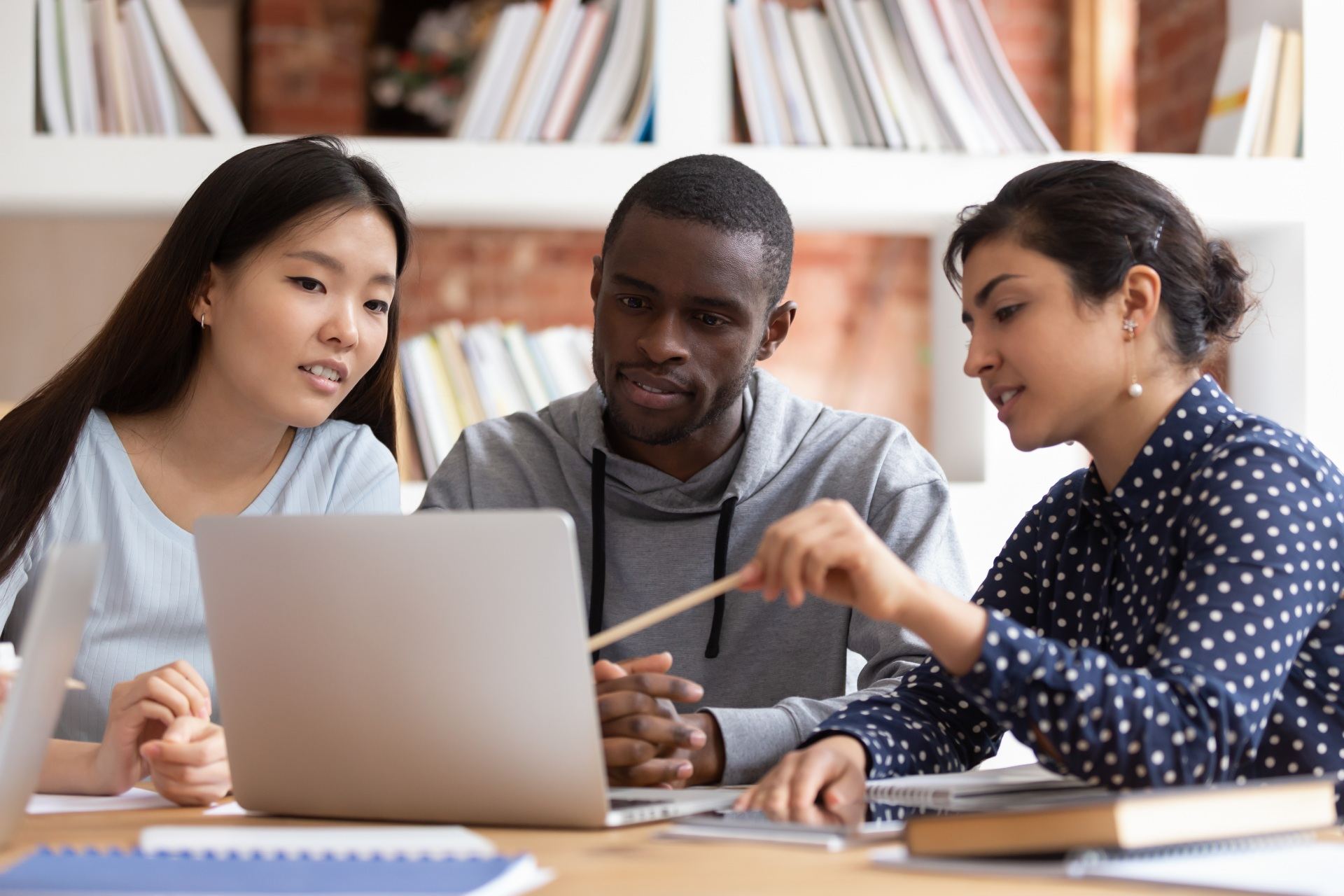 Multiethnic diverse students sit at desk look at laptop screen