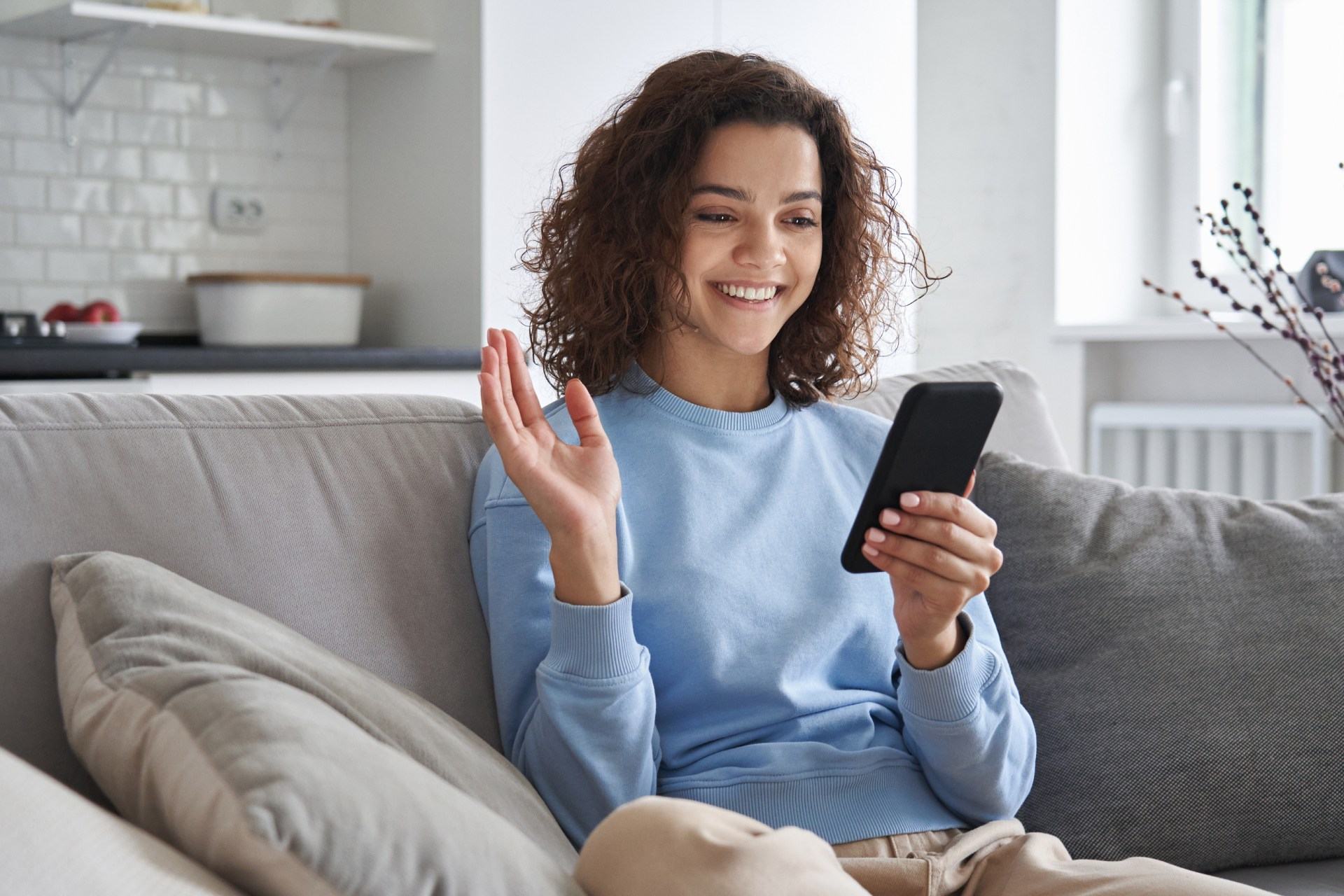 Happy hispanic teen girl waving hand using smartphone app