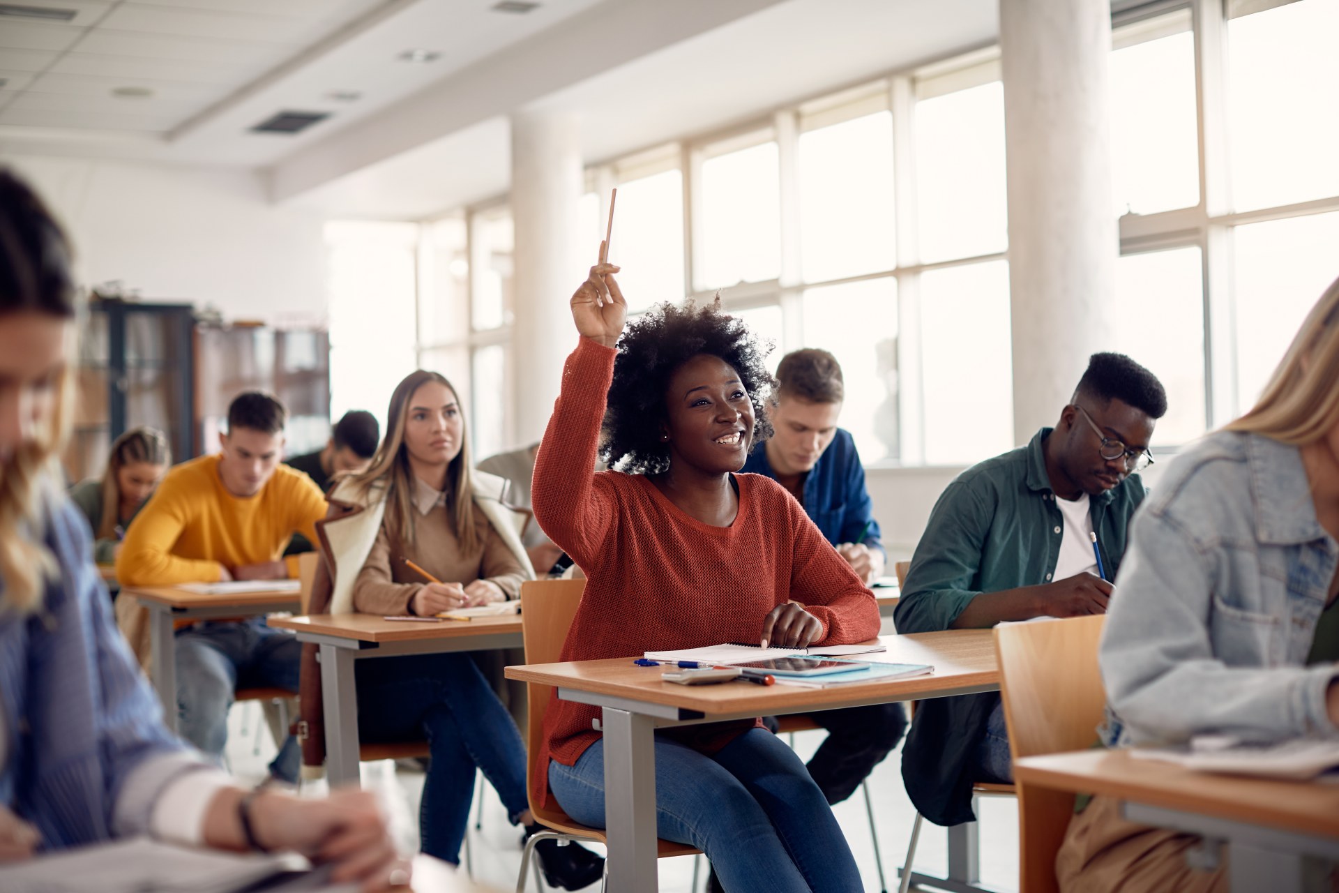 Happy African American student raising her hand to ask a question during lecture in the classroom.