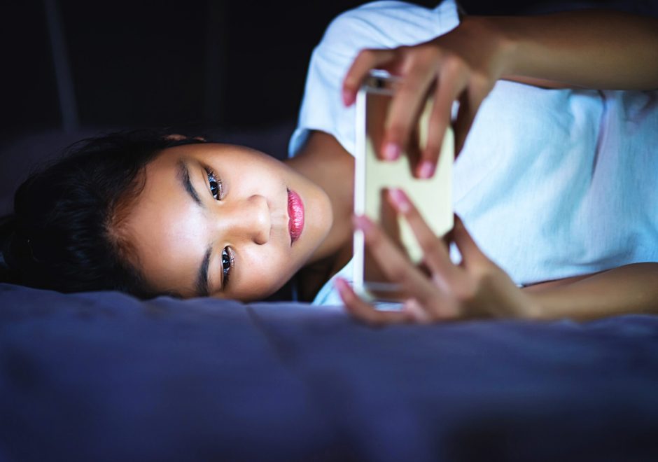 teen girl lying in bed at night and using smart phone